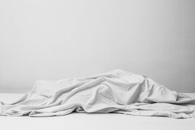 Close-up of white blanket on bed against wall
