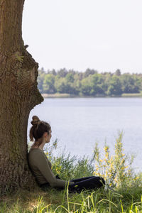 Rear view of woman sitting on rock by lake