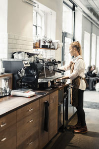 Full length of female barista using coffee machine at cafe