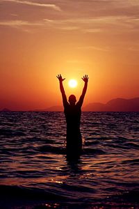 Silhouette of woman in sea at sunset