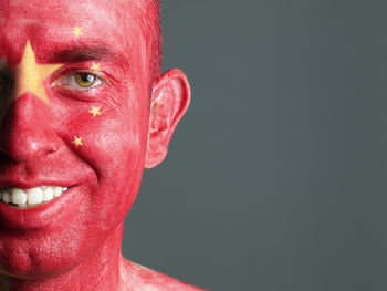 Close-up portrait of smiling man with chinese flag body paint against gray background