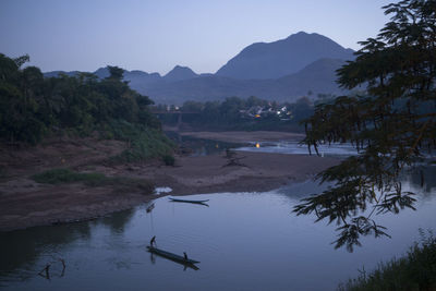 Scenic view of river by mountains at dusk