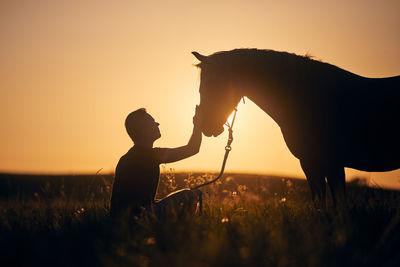 Silhousette of man stroking of therapy horse. 