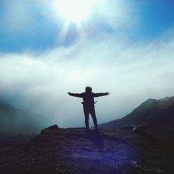 Person with arms outstretched standing on mountain against sky