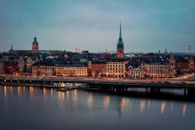 Illuminated buildings by river against sky in city