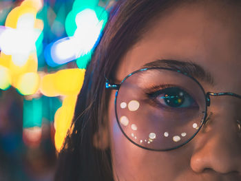 Cropped portrait of woman wearing eyeglasses with reflection in illuminated city at night