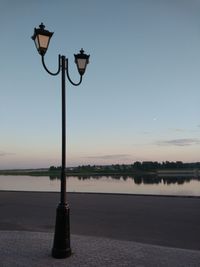 Street light by lake against clear sky during sunset