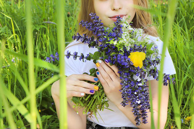 Midsection of girl holding flowers standing amidst plants