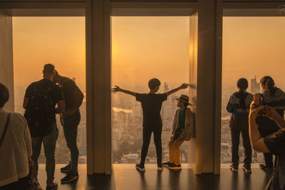 People standing by window at sunset