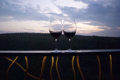 Close-up of wineglass on table against sunset sky