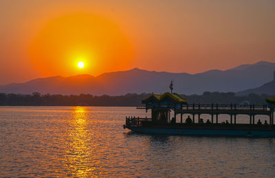 Silhouette boat in lake against orange sky