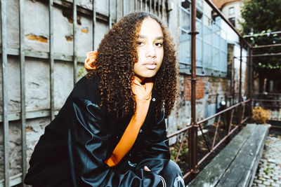 Portrait of teenage girl with curly hair sitting against wall