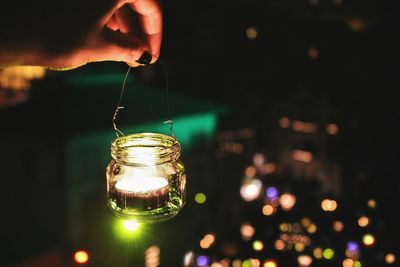 Close-up cropped hand holding lit tea light candle at night