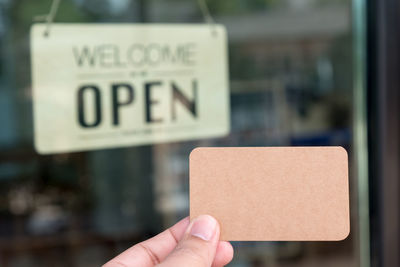 Cropped image of hand holding business card against information sign seen through glass window