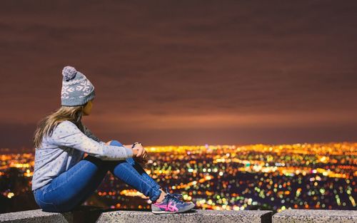 Full length of woman sitting on building terrace against illuminated city at sky high mount dandenong