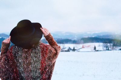 Rear view of woman wearing hat while standing on snow covered field against sky