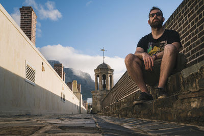 Low angle view of man sitting against building