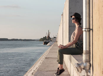Full length of woman sitting on wall by river