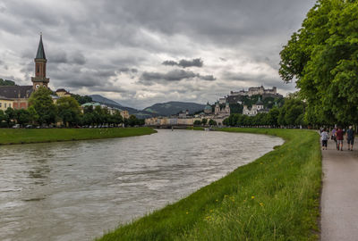 View of buildings by river against cloudy sky