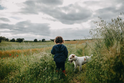 Rear view of a child and dog standing on field