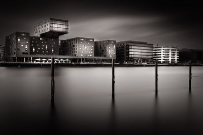 Wooden posts on river against buildings in city at night