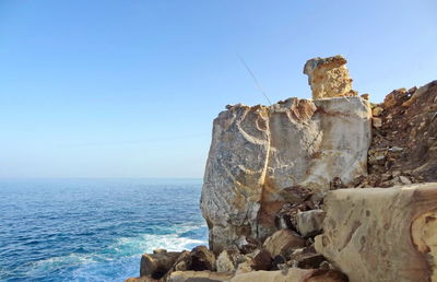 Rock formation by sea against clear blue sky