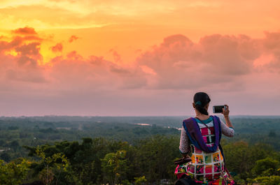 Rear view of man photographing against sky during sunset