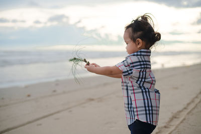 Boy holding umbrella on beach against sky