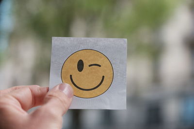 Close-up of hand holding anthropomorphic smiley face on paper