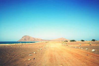 Scenic view of desert road against clear blue sky