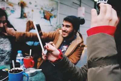 Cropped image of woman holding smart phone while sitting by friends