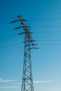 Low angle view of electricity pylon against blue sky