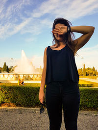 Young woman standing at park against sky