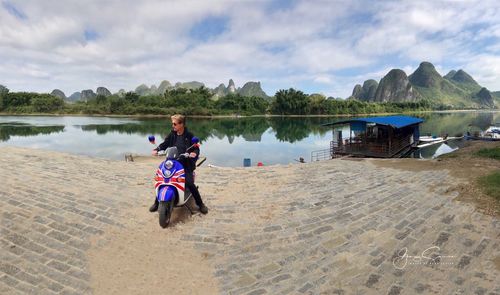 People sitting on riverbank against sky