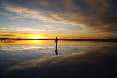 Silhouette man standing on beach against sky during sunset