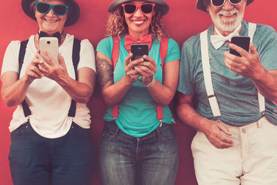 Smiling people using smart phones against wall