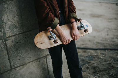 Midsection of woman holding skateboard while standing against wall