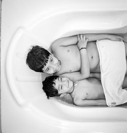 Portrait of naked siblings lying in bathtub