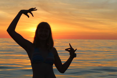 Woman standing by sea against sky during sunset