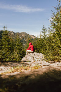 Woman sitting by plants against sky