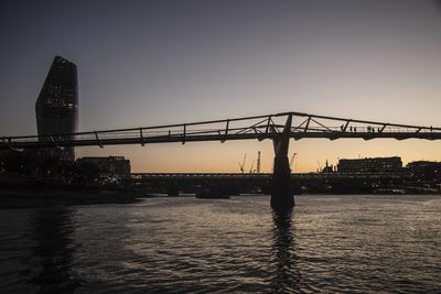 Silhouette of bridge over river against buildings