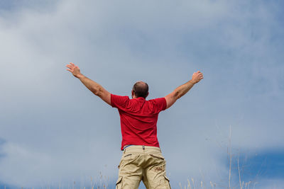 Rear view of man with arms outstretched standing against cloudy sky