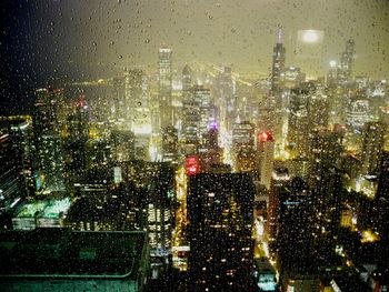 Illuminated city seen through wet window at night