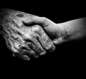 Cropped image of grandfather holding hand of grandson against black background