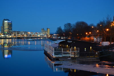 Sea by illuminated city against clear sky at dusk