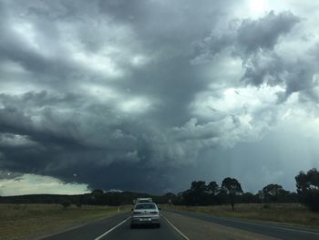 Cars on highway against cloudy sky