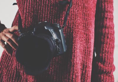 Midsection of woman with camera standing against white background