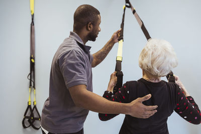 Male caregiver helping senior stretching resistance band in nursing home
