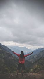 Rear view of man with arms outstretched standing on mountain against cloudy sky