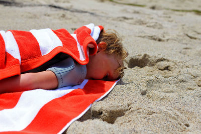 Boy with towel sleeping at beach on sunny day